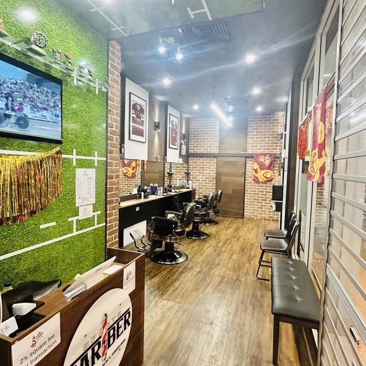 Inside Sports Barber: astroturf feature wall, sport on the TV, trophies and barber chairs down the room