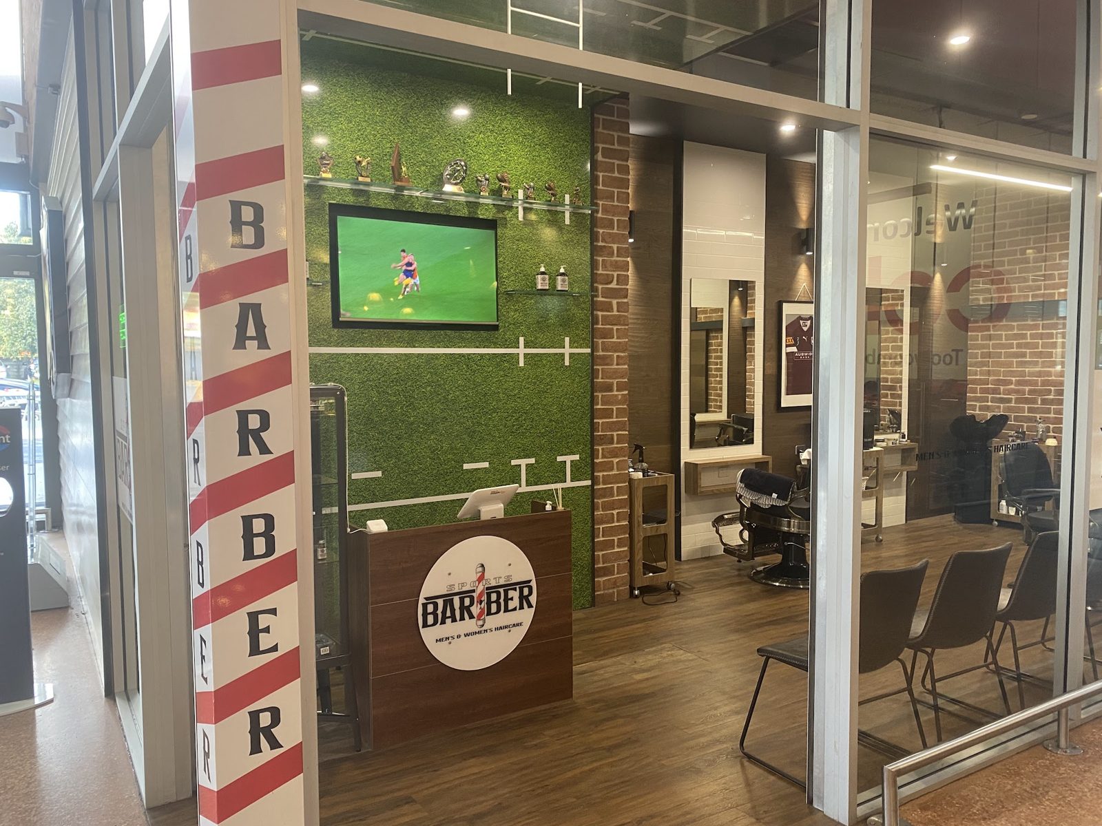 Reception desk, astroturf wall and TV inside Sports Barber
